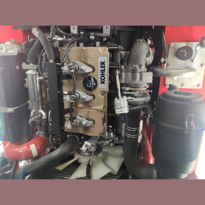 A close-up view of a Kohler engine with various mechanical components, hoses, and metal parts visible against a red background.